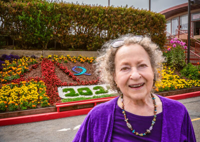 Eve Meyer, former executive director of San Francisco Suicide Prevention (SFSP), stands in front of a flower installation adorned with the purple and teal Suicide Prevention Awareness Ribbon at the Golden Gate Bridge.